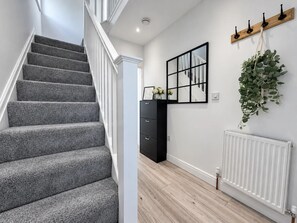 A staircase with grey carpet, a black cabinet, a mirror, and a hanging plant. - Family Home | Free Secure Parking | Pets Allowed - Pass the Keys (Salford)