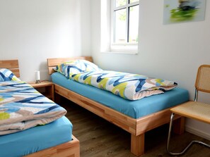 A room with two wooden beds, a chair, a bedside table, and a window. - Paula Apartment 2 (Wyk auf Foehr)