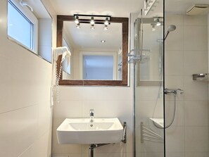 Ein modernes Badezimmer mit Duschkabine aus Glas, einem weißen Waschbecken und einem Spiegel mit Beleuchtung darüber.
