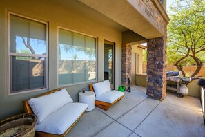 A covered outdoor seating area with two sofas and a small table, a grill, and a tree in the background. - Remodeled modern north Scottsdale Town Home! (Scottsdale)