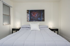 A bedroom with a large bed, two bedside tables, a window, and a wall-mounted abstract painting. - Remodeled modern north Scottsdale Town Home! (Scottsdale)
