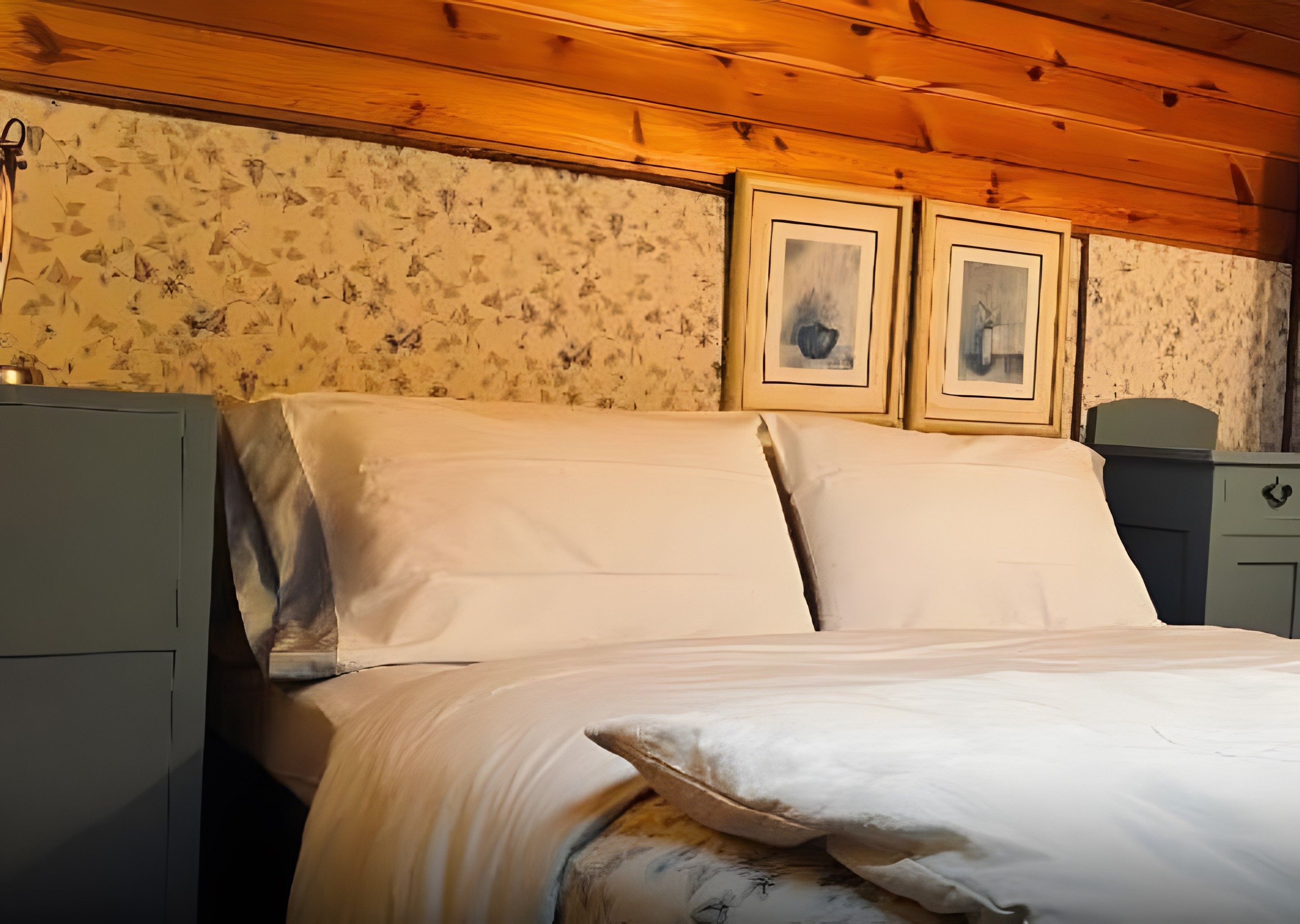 Un letto con lenzuola bianche in una stanza con soffitto in legno e carta da parati floreale.