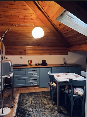 Kompakti keittiö, jossa on puinen katto, ruokapöytä tuoleineen ja pieni matto.