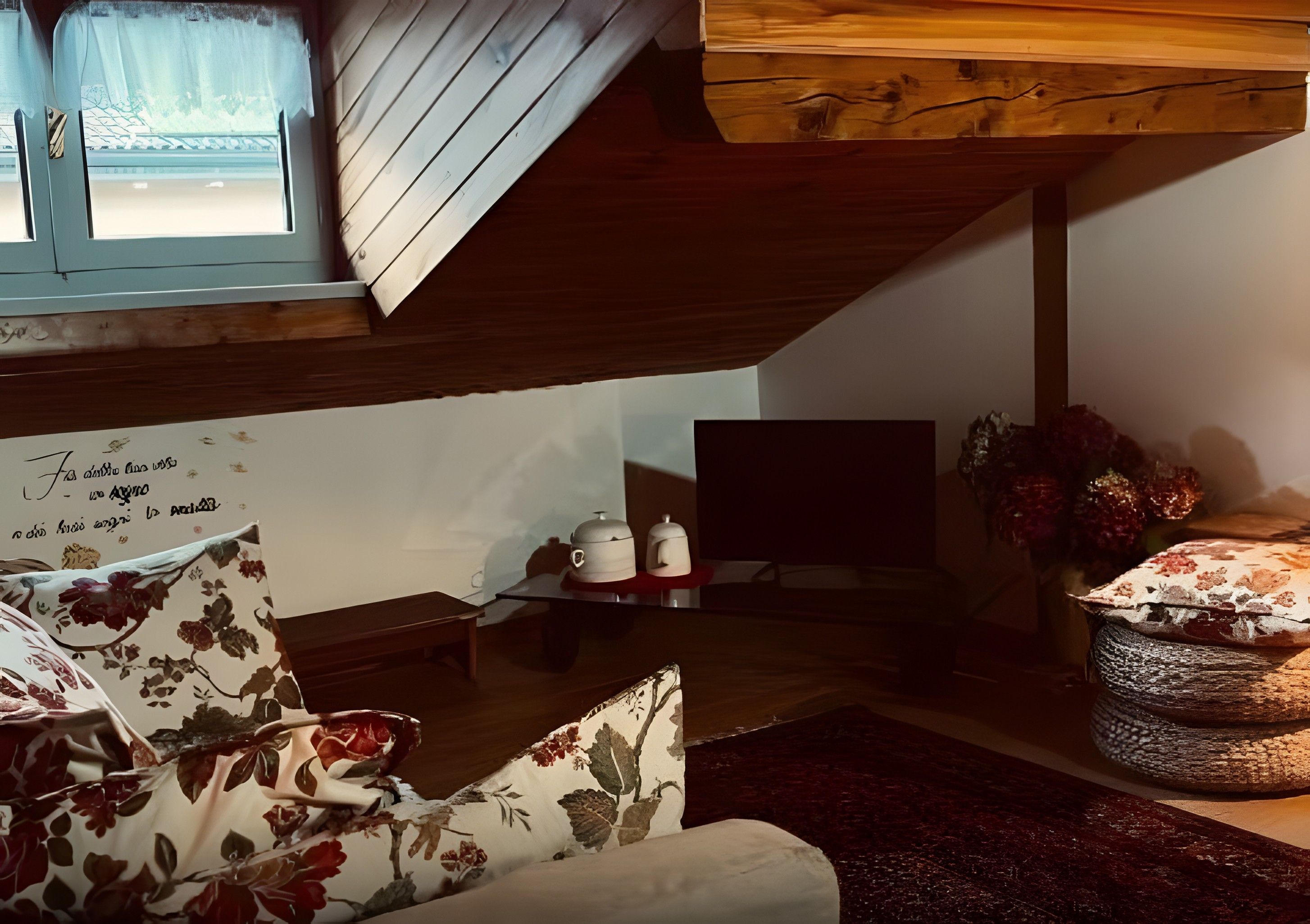 Un salon chaleureux avec un plafond en pente, un canapé recouvert d’un tissu à motifs floraux, une petite table sur laquelle sont posées des théières et un téléviseur.