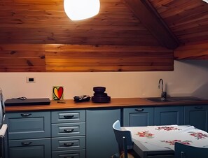 Keittiössä on puupalkit katossa, pesuallas, kukkapintainen pöytäliina ja sininen kaappi, jossa on laatikoita.