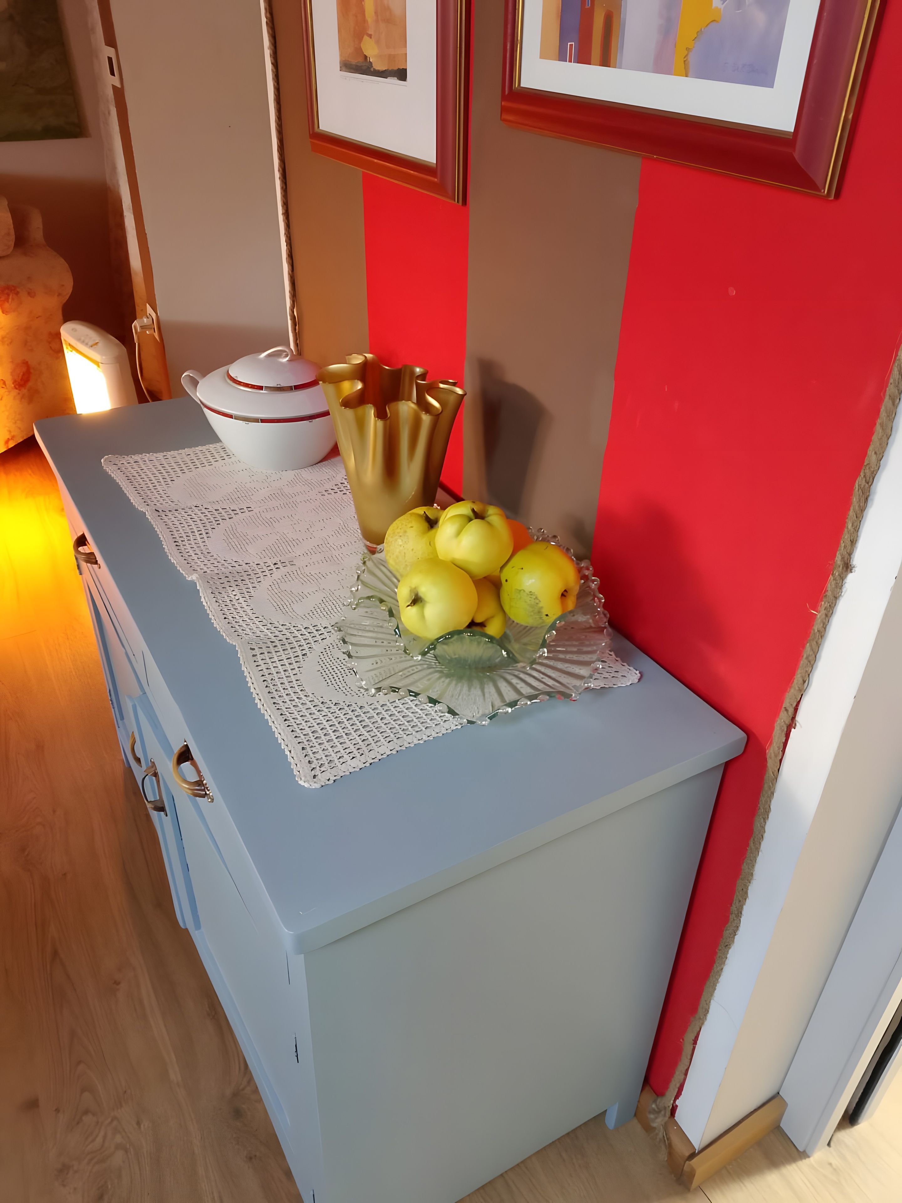 A kitchen counter with a bowl of apples, a white tablecloth, and a gold vase.