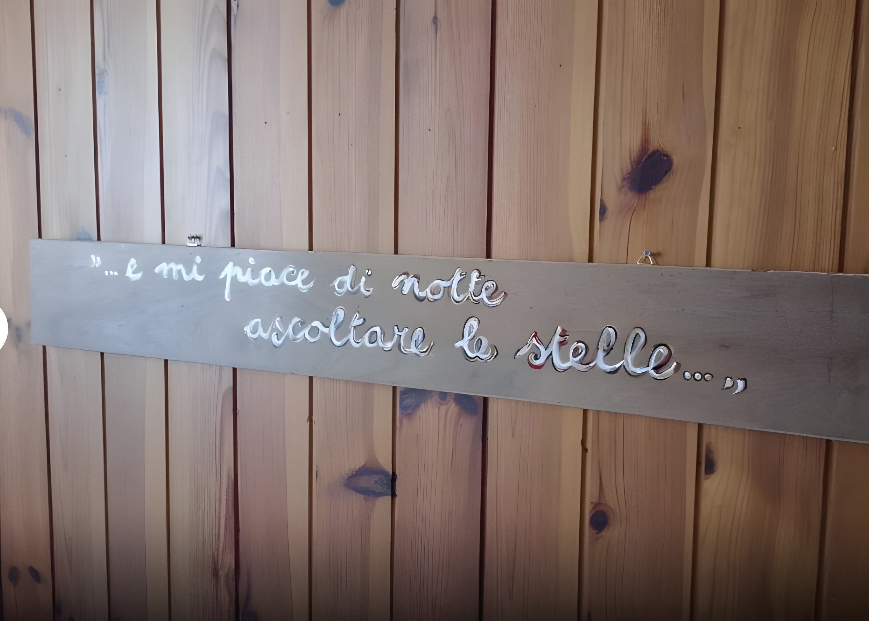 Una pared de madera con una placa de metal que dice '...e mi piace di notte ascoltare la stella...'.