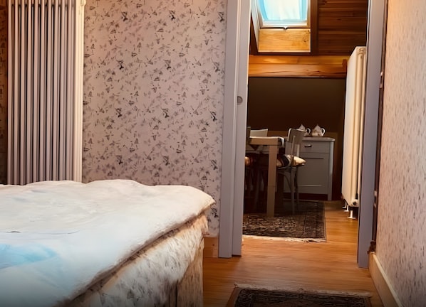 A bedroom with a bed, a window, and a view into a kitchen area.