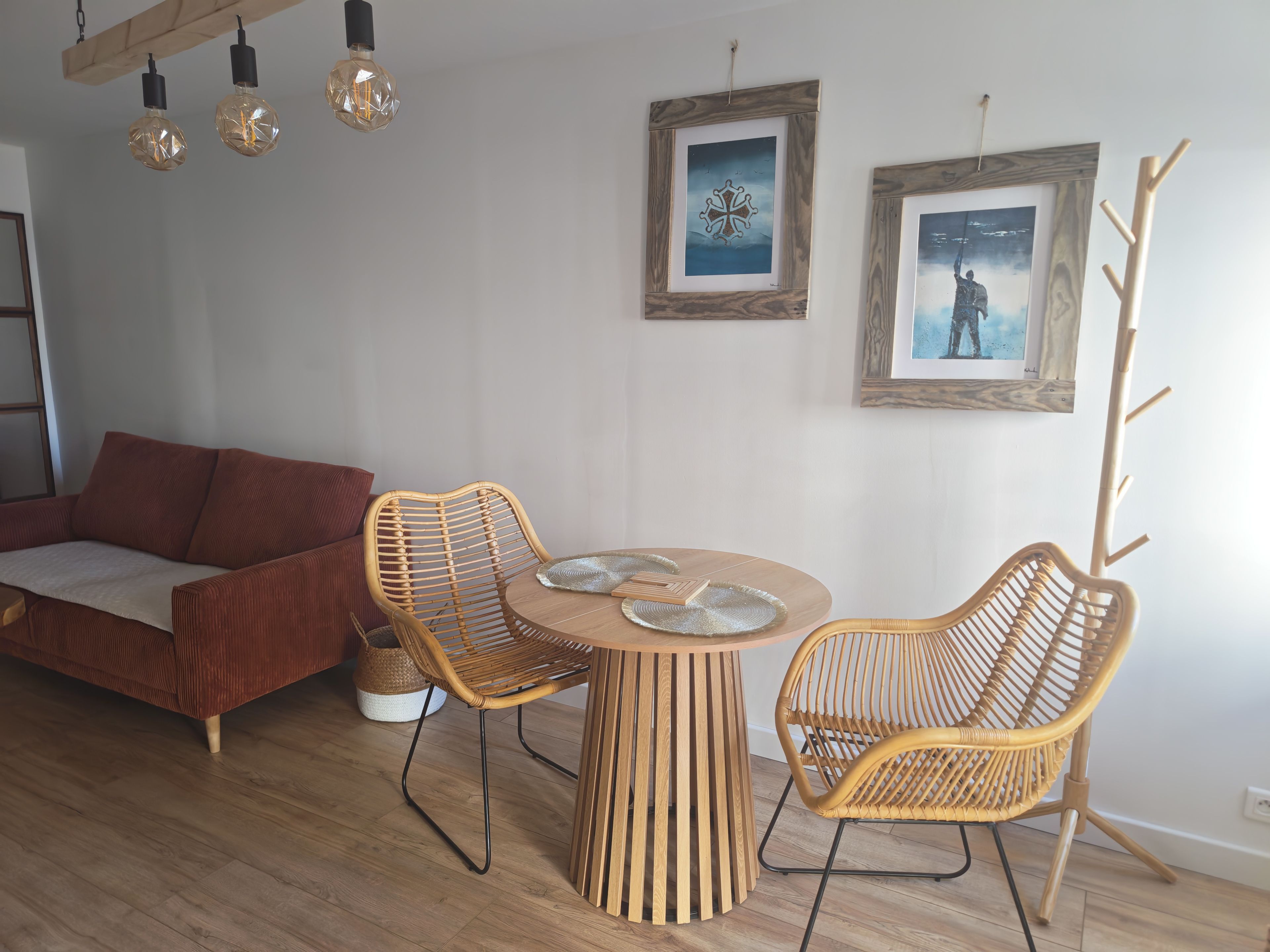 Una sala de estar moderna con un sofá, dos sillones de mimbre, una mesa redonda de madera y dos obras de arte enmarcadas en la pared.