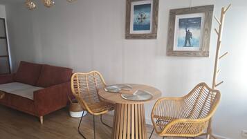 Una sala de estar moderna con un sofá, dos sillones de mimbre, una mesa redonda de madera y dos obras de arte enmarcadas en la pared.