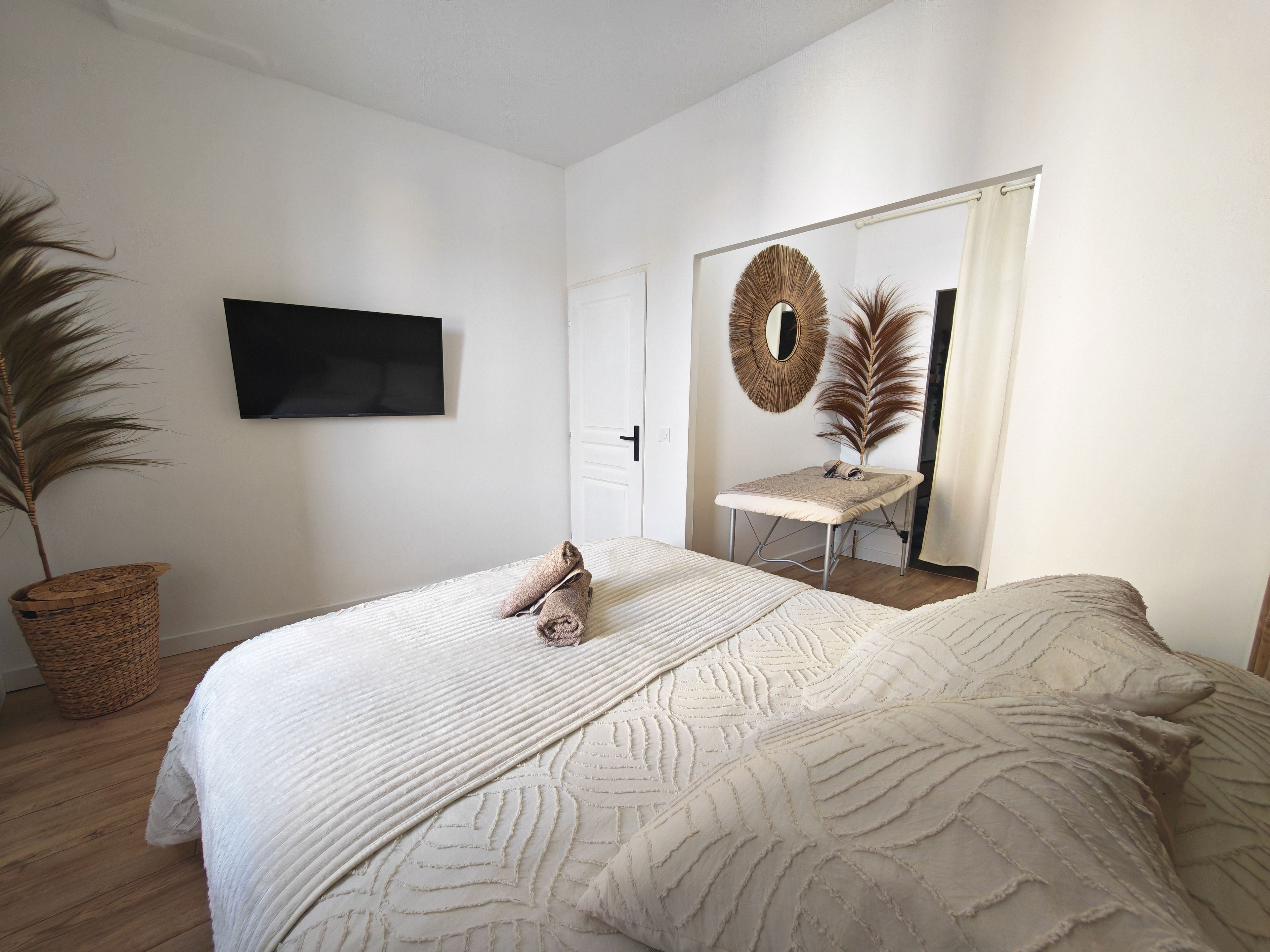 A bedroom with a bed, a flat-screen TV mounted on the wall, a mirror with a decorative frame, and a potted plant.