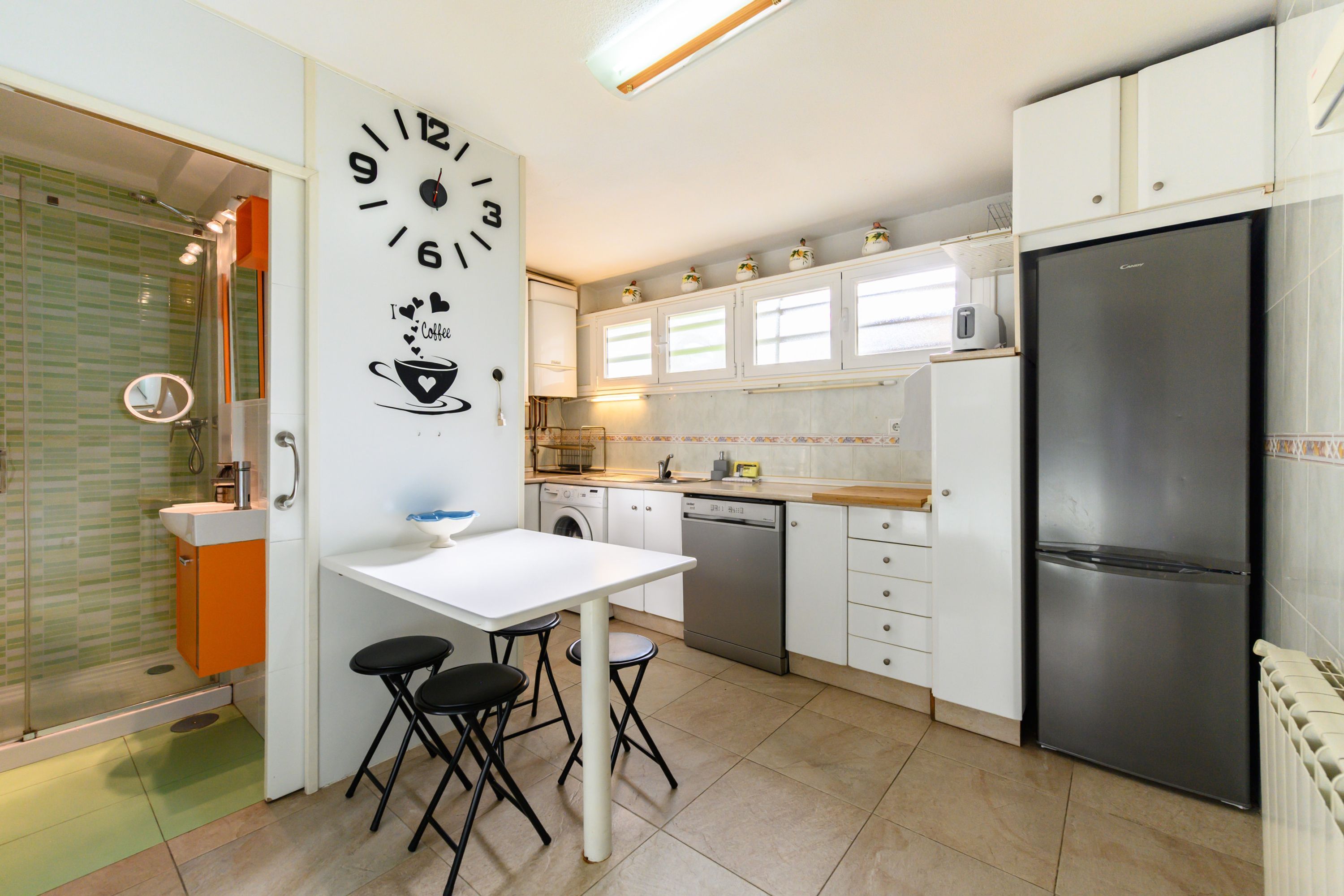 Una cocina moderna con encimera blanca, refrigerador negro y decoración de pared con motivos de café.