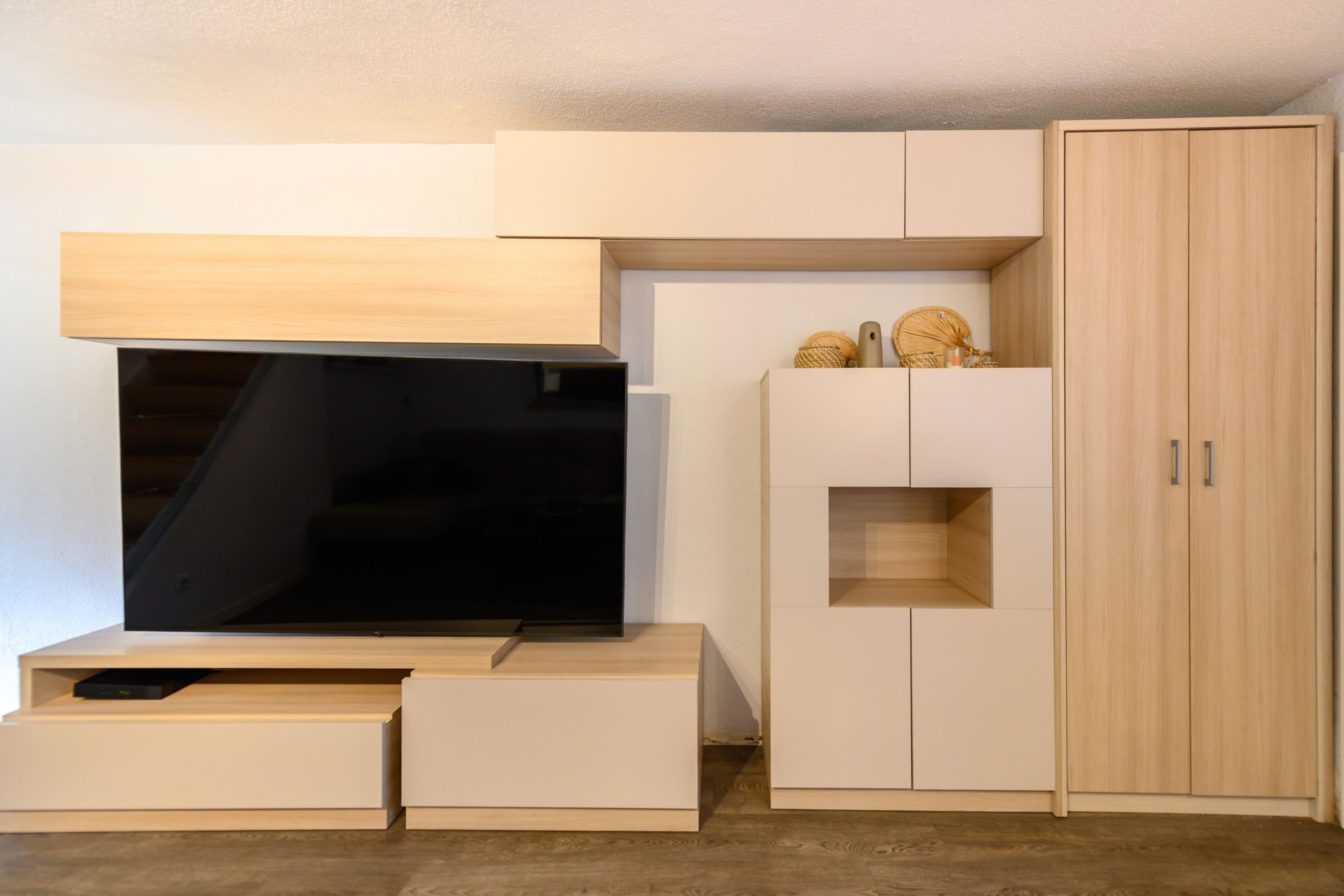 Una habitación moderna y minimalista con muebles empotrados, incluyendo una televisión de pantalla plana, un armario de madera y un ropero.