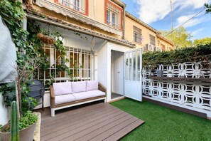 Un patio con un sofá blanco, una terraza de madera y un pequeño césped artificial.