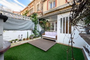 A patio with a wooden deck, a white wall, and a small garden area with potted plants. - M Sab52 Amplio Chalet 3 Dormitorios y Terraza (Madrid)