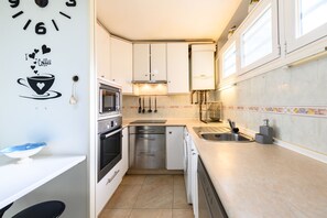Una cocina compacta con gabinetes blancos, lavavajillas, microondas y pileta.