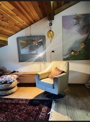 Habitació amb sostre de fusta, una cadira moderna, una catifa, un quadre i una làmpada.