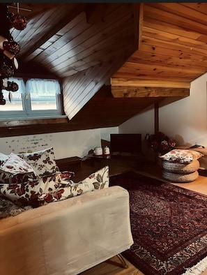 A cozy loft bedroom with a sloped ceiling, a bed with floral pillows, a dark patterned rug, and a small table with decorative items. - Apartment 'Al Piccolo Principe - Volpe' with Mountain View, Shared Garden and Wi-Fi (Cles)