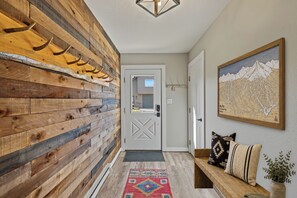 A hallway with a wooden wall, a door, a rug, a bench with pillows, and a framed map on the wall. - Summit & Stream at Candlelight Meadows (Big Sky)