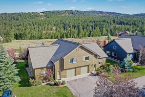 A residential area with houses, a well-maintained lawn, and a forested hill in the background. - Summit & Stream at Candlelight Meadows (Big Sky)