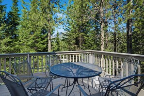 A deck with a round table and chairs, surrounded by a railing, overlooking a forested area. - Hidden Village Haven (Big Sky)