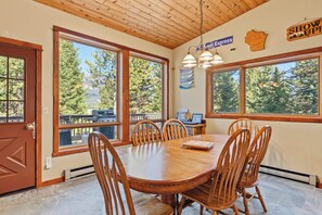 A dining area with a wooden table and chairs, large windows with a view of trees, and a sign that says 'SHOW UP!' - Hidden Village Haven (Big Sky)