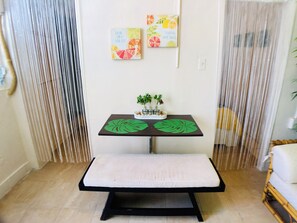 Ein Zimmer mit einem Bett, einem kleinen Tisch mit einer Pflanze und zwei Wandbildern.