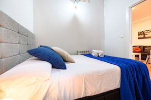 Una cama con cabecera, almohadas y una manta azul.