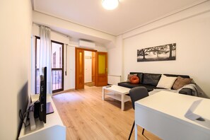 A living room with a sofa, a coffee table, and a TV. There is a door leading to a balcony. - M Adu151a Piso 2 Dormitorios en Sol Centro de M (Madrid)