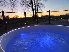 A hot tub with a blue light, surrounded by a fence and string lights, with a sunset in the background.