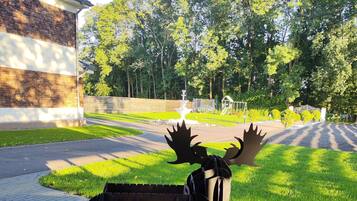 A sculpture of a moose in a park setting with a paved walkway, trees, and a building in the background.