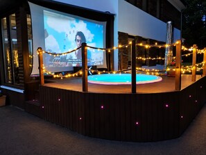 Ett utomhusområde för underhållning med en pool, en stor skärm och ljusslingor.