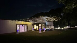 Un edificio con un espacio al aire libre techado, varias mesas con sombrillas y una fuente de agua al fondo.