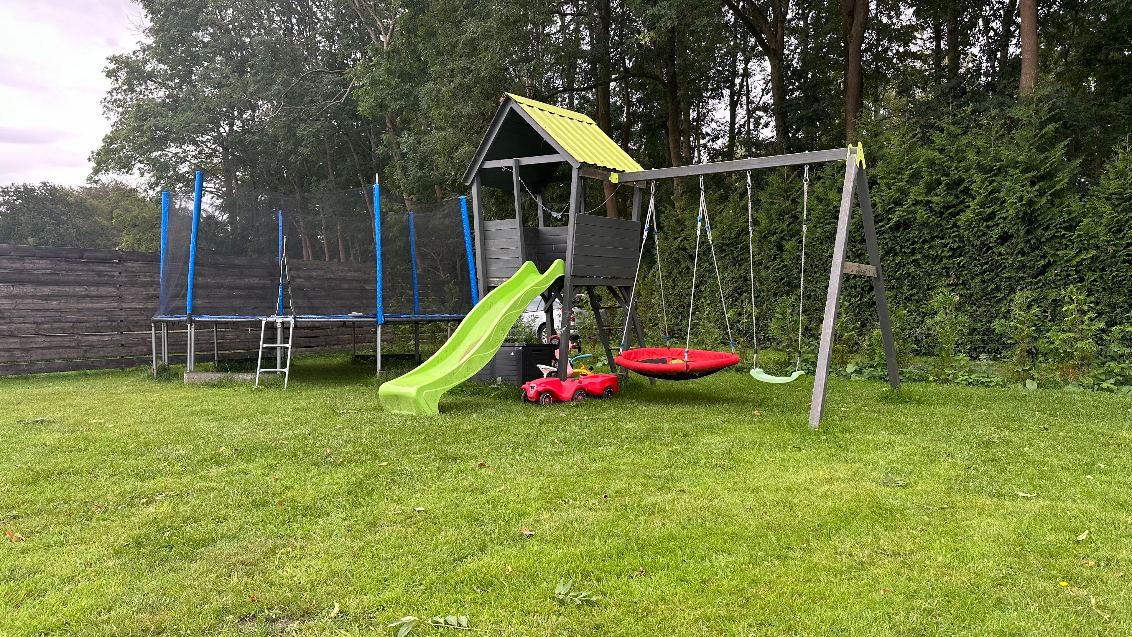 En lekplats med en rutschkana, gungor och en liten röd leksaksbil.