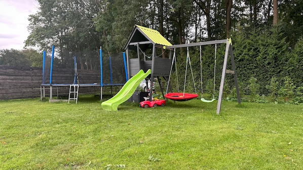 En lekplats med en rutschkana, gungor och en liten röd leksaksbil.