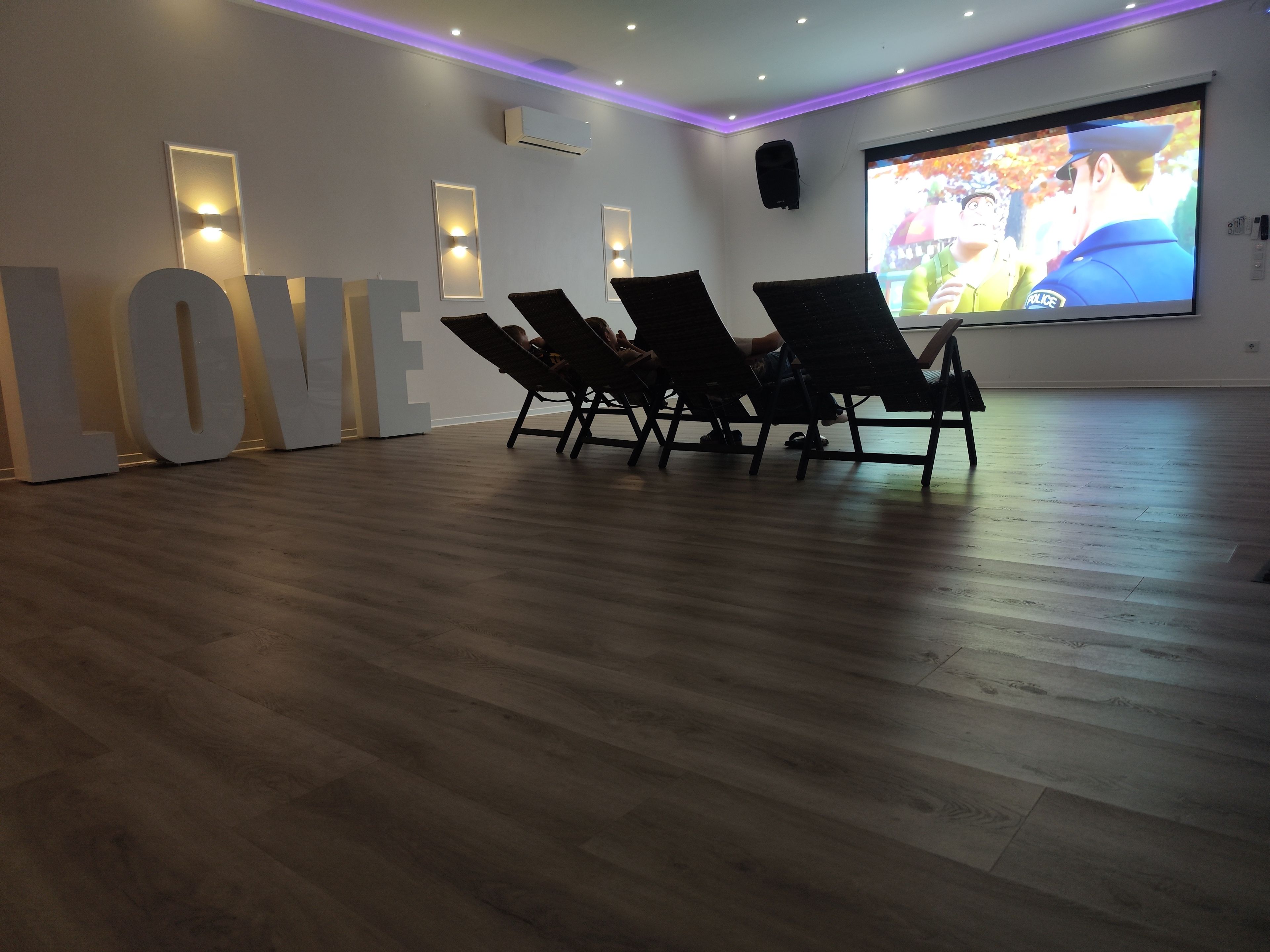 Ein Zimmer mit einem großen 'LOVE'-Schild, einer Projektionsleinwand und vier Lounge-Sesseln.