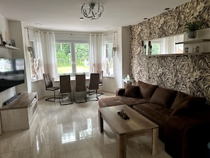 Una sala de estar moderna con sofá, mesa de centro, televisor y un comedor con sillas y una mesa.