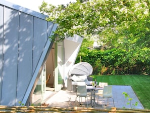 A modern outdoor patio with a dining table and chairs, a white umbrella, and a glass door leading to a covered area. - Vakantievilla Sint Maartenszee (Sint Maartensvlotbrug)