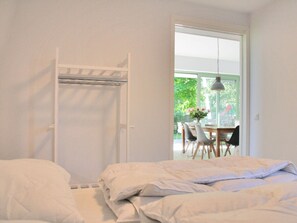 A bedroom with a bed, a white wardrobe, and a view of an outdoor dining area through a glass door. - Vakantievilla Sint Maartenszee (Sint Maartensvlotbrug)