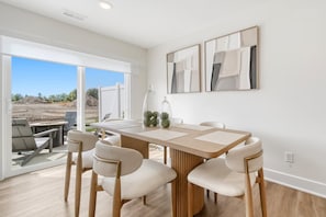 A modern dining area with a long table, six chairs, and a view of an outdoor construction site. - Hot Tub - Trail Access - Near Lake Michigan (South Haven)