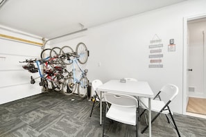A room with a white table and chairs, a bicycle rack with multiple bikes, and a door with a sign. - Hot Tub - Trail Access - Near Lake Michigan (South Haven)
