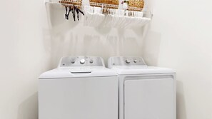 Een voorzichtige blik op een witte wasruimte met twee gestapelde wasmachines en een droogrek erboven.