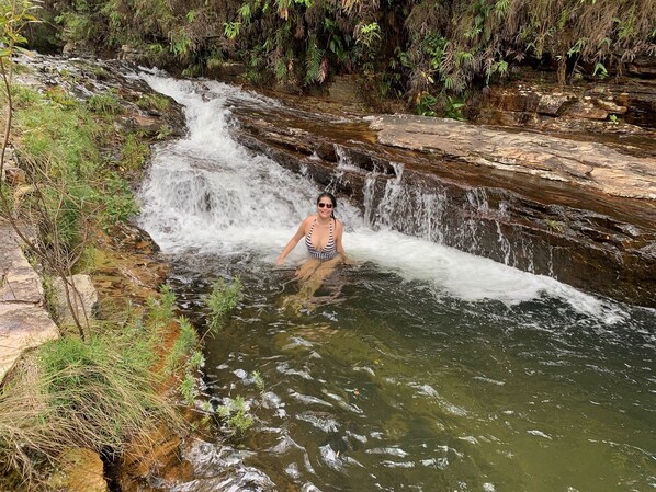 A person in a swimsuit standing in a natural water setting with a waterfall.