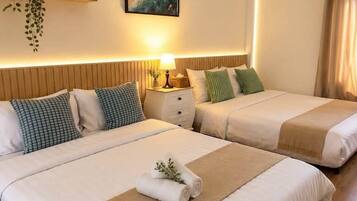 A hotel room with two beds, a bedside table with a lamp, a wall-mounted shelf with a plant, and a painting.