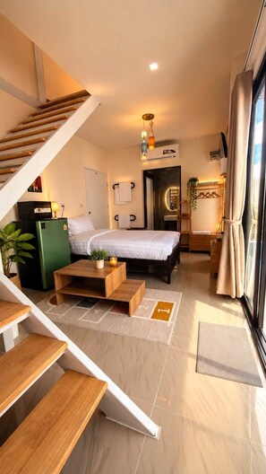 A modern hotel room with a bed, a desk, a chair, a small table, a plant, a mirror, a window with curtains, and a staircase. - Thana Bangsaen Poolvilla  (Tambon Saen Suk)
