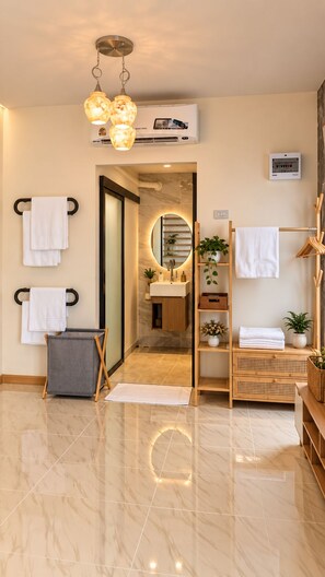 A modern bathroom with a marble floor, a round mirror, a towel rack, a sink, and a shower area. - Thana Bangsaen Poolvilla  (Tambon Saen Suk)