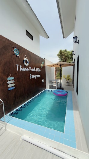 Una piscina con borde de azulejos azules y blancos, una silla de descanso y una planta en maceta.