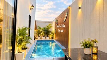 A modern outdoor pool area with a wooden wall, potted plants, and a bench.