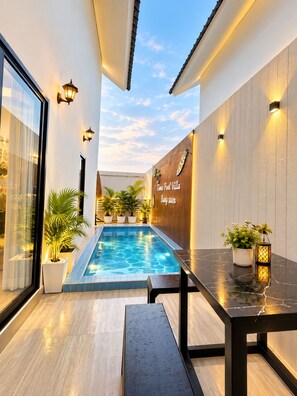 A modern outdoor pool area with a wooden wall, potted plants, and a bench. - Thana Bangsaen Poolvilla  (Tambon Saen Suk)