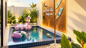 A swimming pool area with a wall-mounted sign, a large umbrella, and inflatable rings.